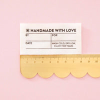 A cream colored label on a scalloped edge ruler against a pink background.