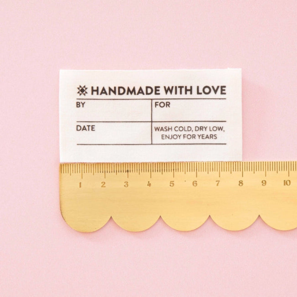A cream colored label on a scalloped edge ruler against a pink background.