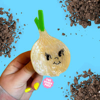 Hand holding a novelty onion-shaped clip with a face design against a blue background with soil.