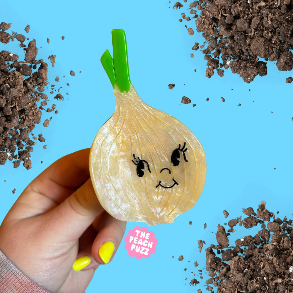 Hand holding a novelty onion-shaped clip with a face design against a blue background with soil.