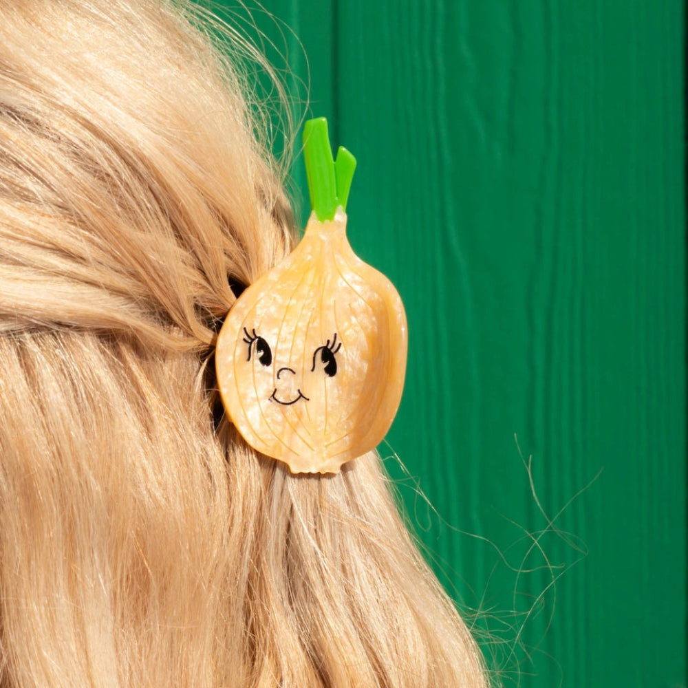 Hair clip shaped like a cartoon onion with a face on a person's hair against a green background