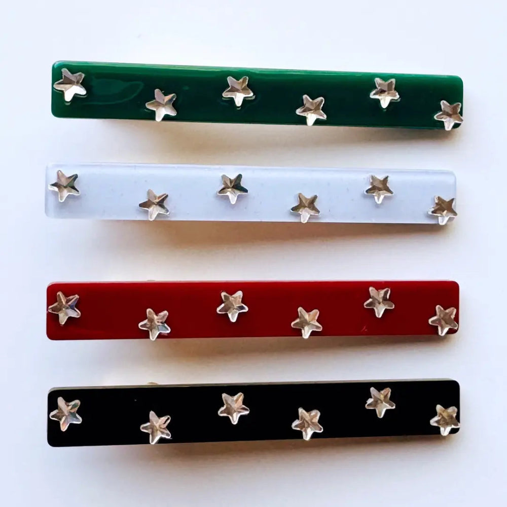 Four rectangular hair barrettes with silver star-shaped studs, shown in green, white, red, and black on a plain white background.