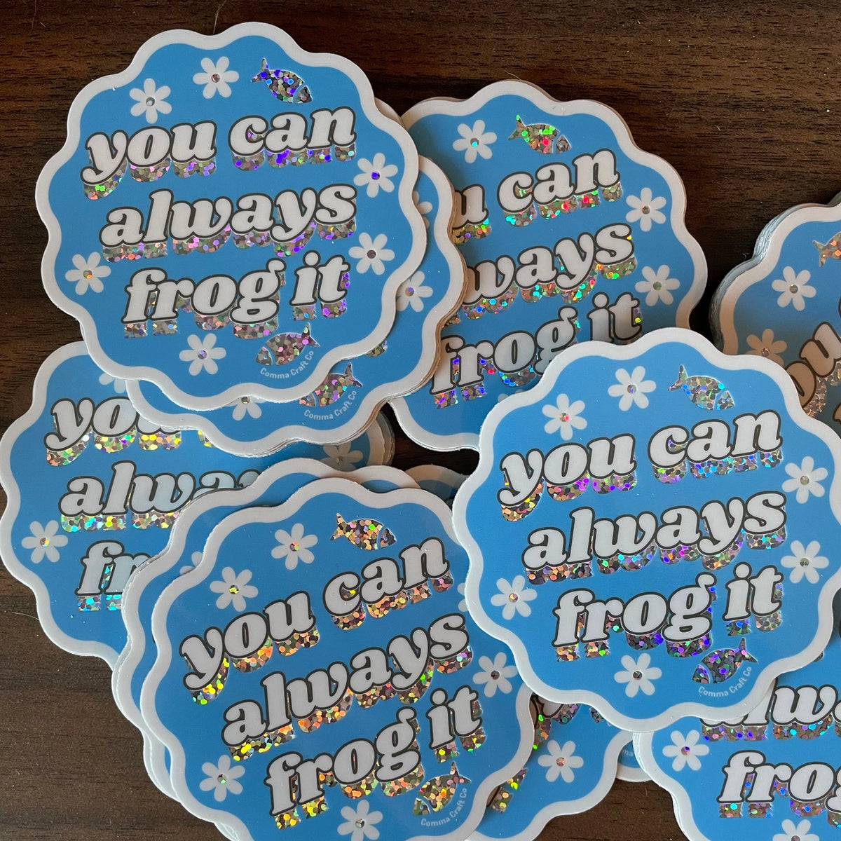 Stack of blue stickers with text 'you can always frog it' on a wooden surface.