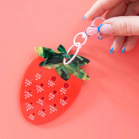 A hand  holds a strawberry-shaped tool for measuring hook sizes with labeled holes in white text. 