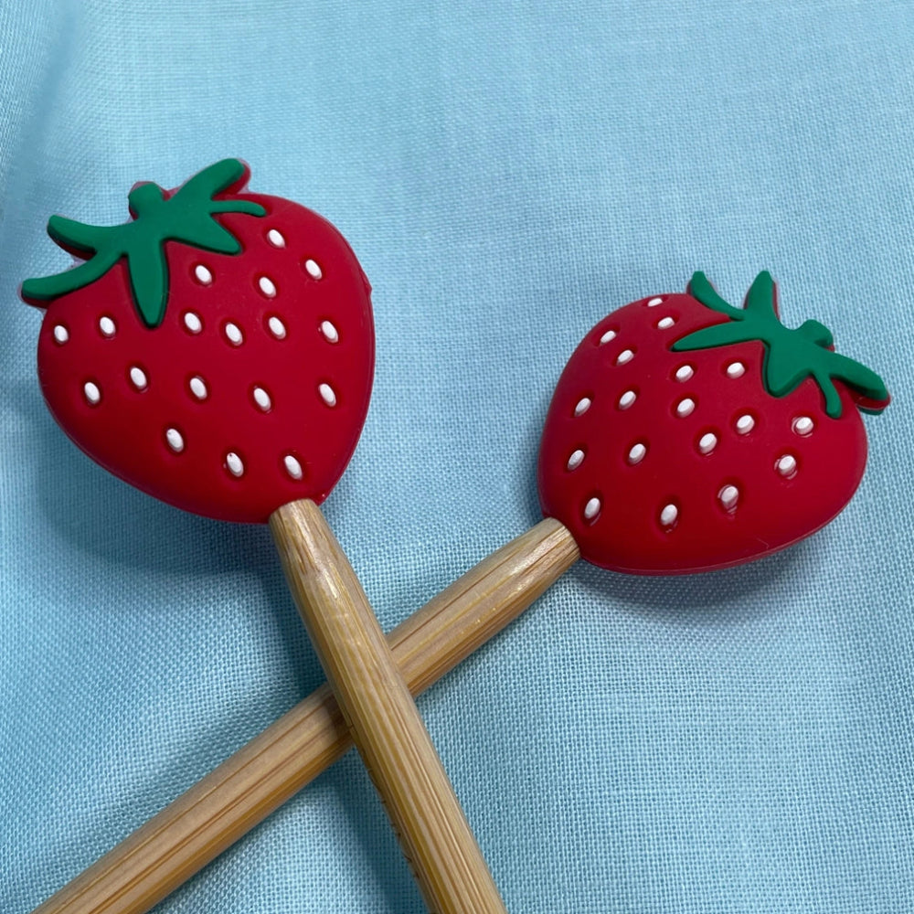 Two strawberry-shaped silicone ends on needles on a light blue background.