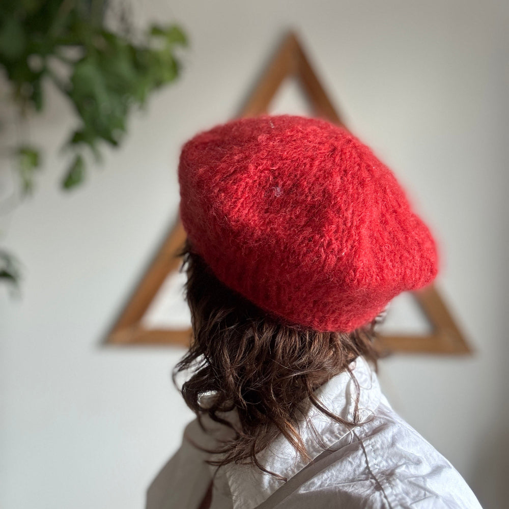 Person wearing a red knitted hat with a white wall and plant in the background