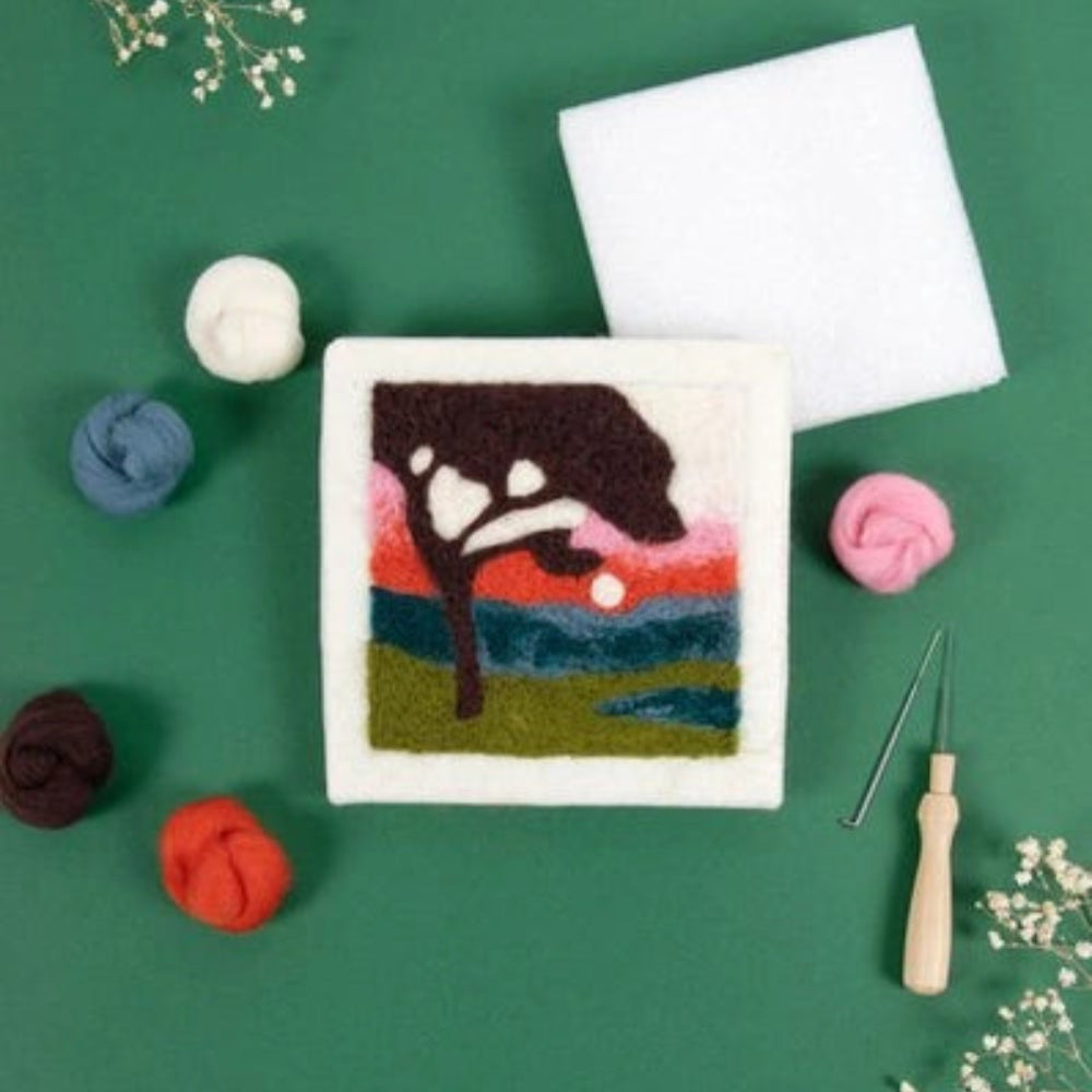 Felted canvas with a black tree design on a green background with fabric and embroidery tools.