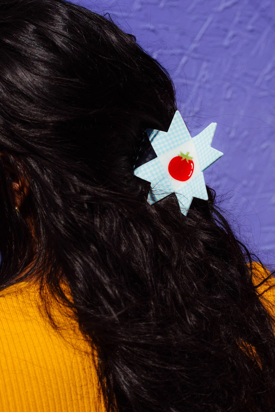 Person with a star-shaped hair clip featuring a red tomato design against a purple textured background