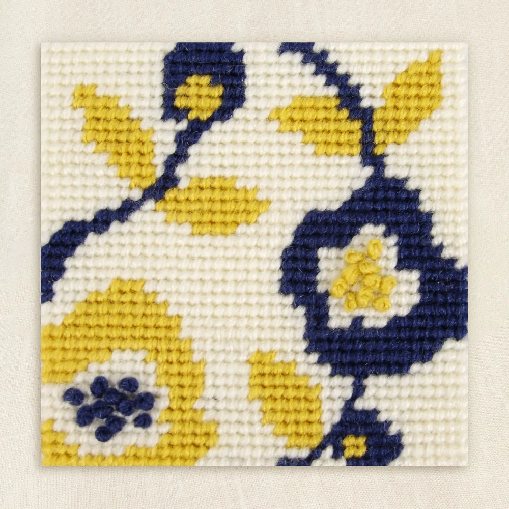 Needlepointed floral design with yellow and blue flowers on a white background