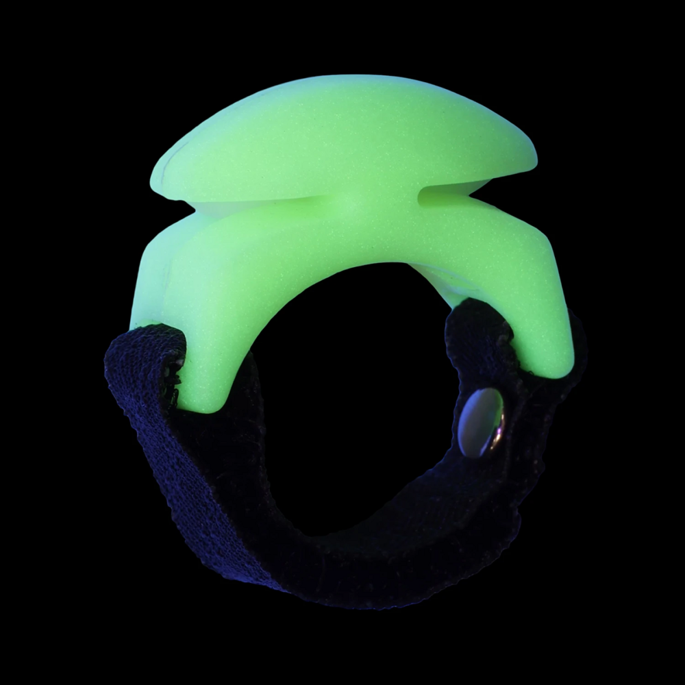 A greenish-glowing plastic ring-shaped device with hidden blades on the sides, a black textured strap and a silver metal snap button, shown in a pitch black background.