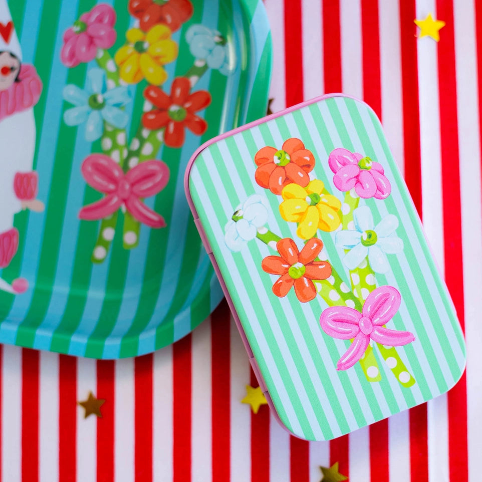 Colorful paper plates and tin with floral and bow designs on a red and white striped background.