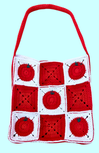 A handmade crocheted shoulder bag featuring a red and white granny square pattern with tomato motifs, set against a solid light blue background.