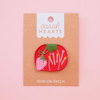 Embroidered red tomato-shaped patch with colorful pins and a pink strawberry on "Sarah Hearts" packaging.
