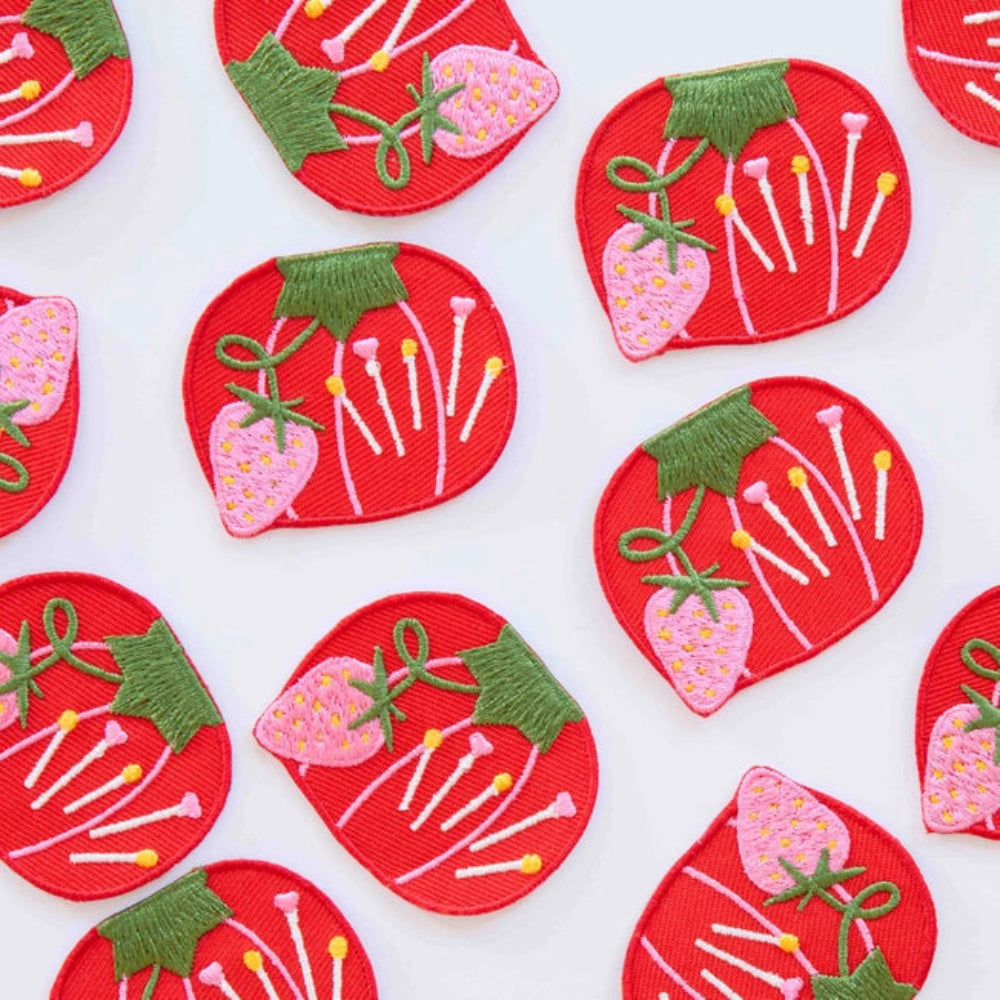 Embroidered red tomato-shaped patches with colorful pins and a pink strawberries, against a white background