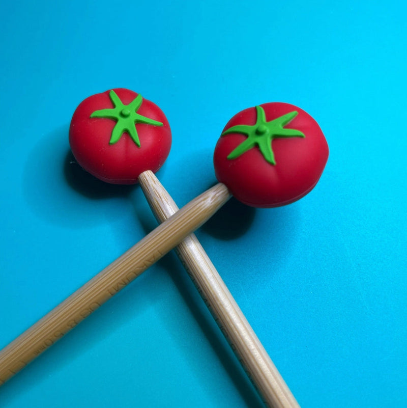 Two wooden needles with tomato-shaped ends on a blue background.