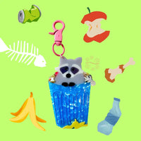 Keychain of a raccoon in a trash can on a green background with random trash items