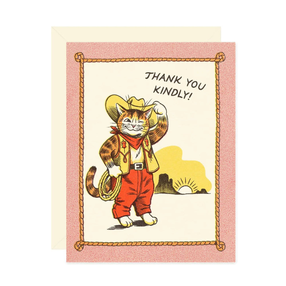 A card with an illustration of a winking cat in western style outfit tipping their hat. They stand in front of a sunset with mountains in the background, with text that says "Thank You Kindly". The illustration is bordered with a rope illustration and pink background. A beige envelope is behind the card.