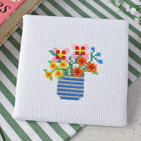 Cross-stitched design of a vase with flowers on a white fabric background