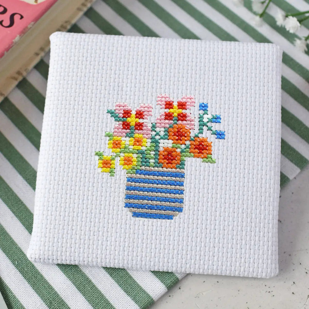 Cross-stitched design of a vase with flowers on a white fabric background