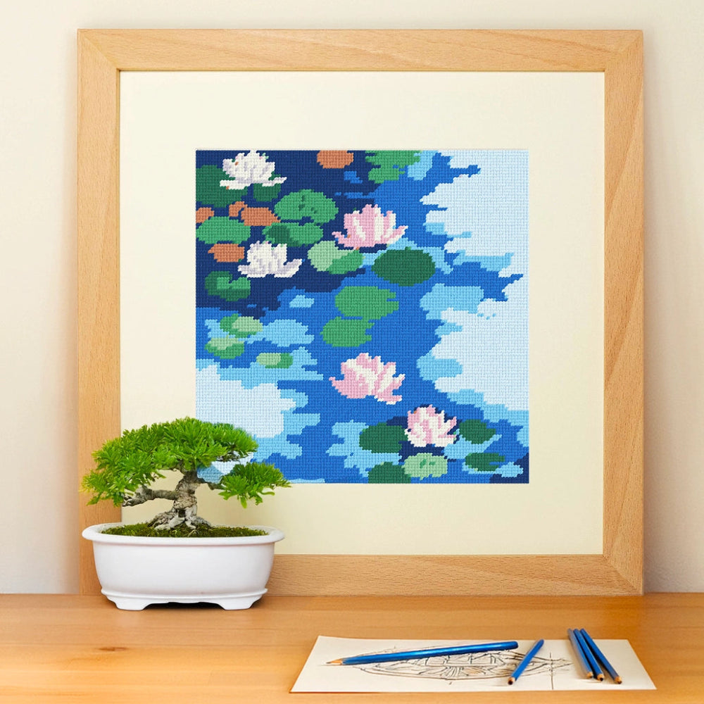 Framed needlepoint artwork with a floral design resting on a wooden table against a white background