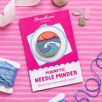 Hawthorn Magnetic Needle Minder with a wave and mountain scene on a pink background with yarn and sewing tools.