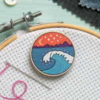 Embroidery hoop with a wave design on fabric, on aida fabric with an embroidery needle and pink thread