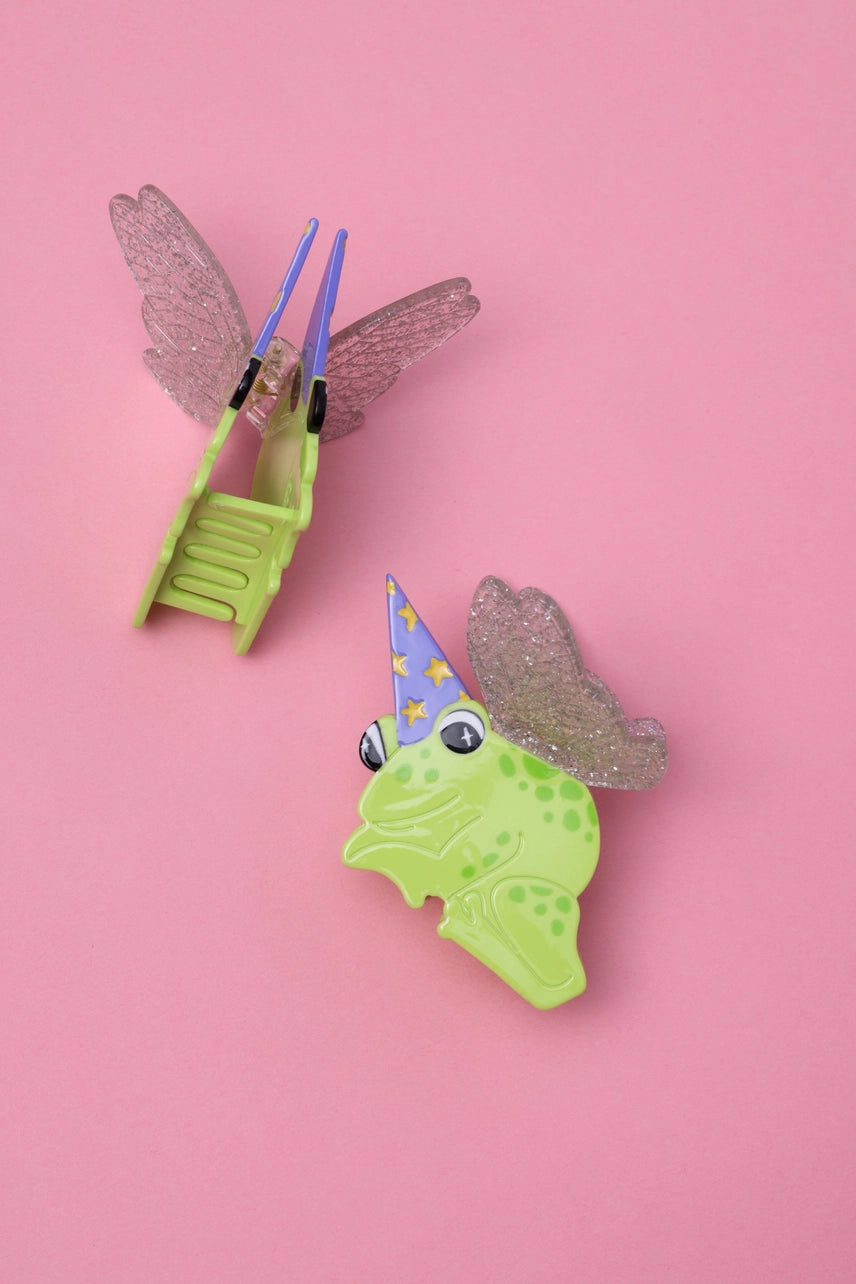 Green frog with party hat and glittery wings on a pink background