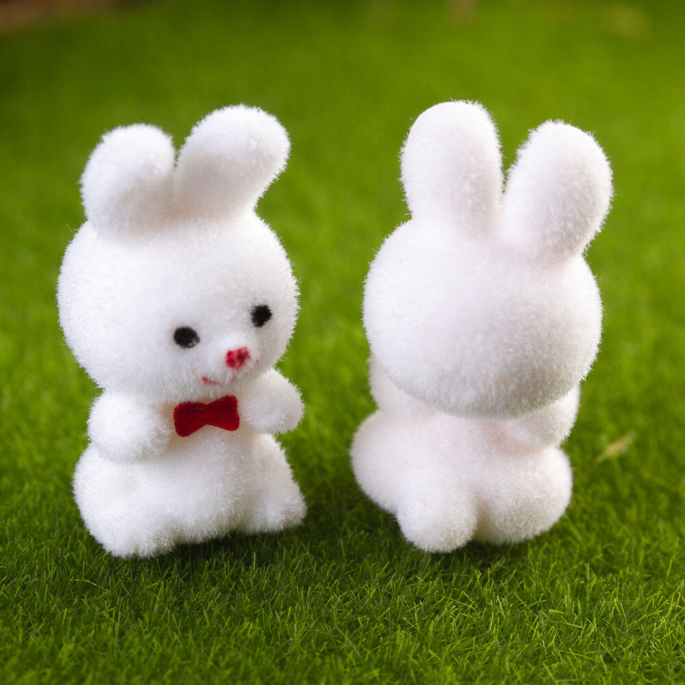 Two white fuzzy bunny figures on a green grass background, one facing forward with a red bow tie and black eyes, and the other showing the back.