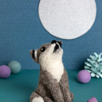 Needle felted wolf toy sitting on a teal surface with a blue background