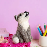 Needle felted wolf toy sitting on a pink surface with a light pink background