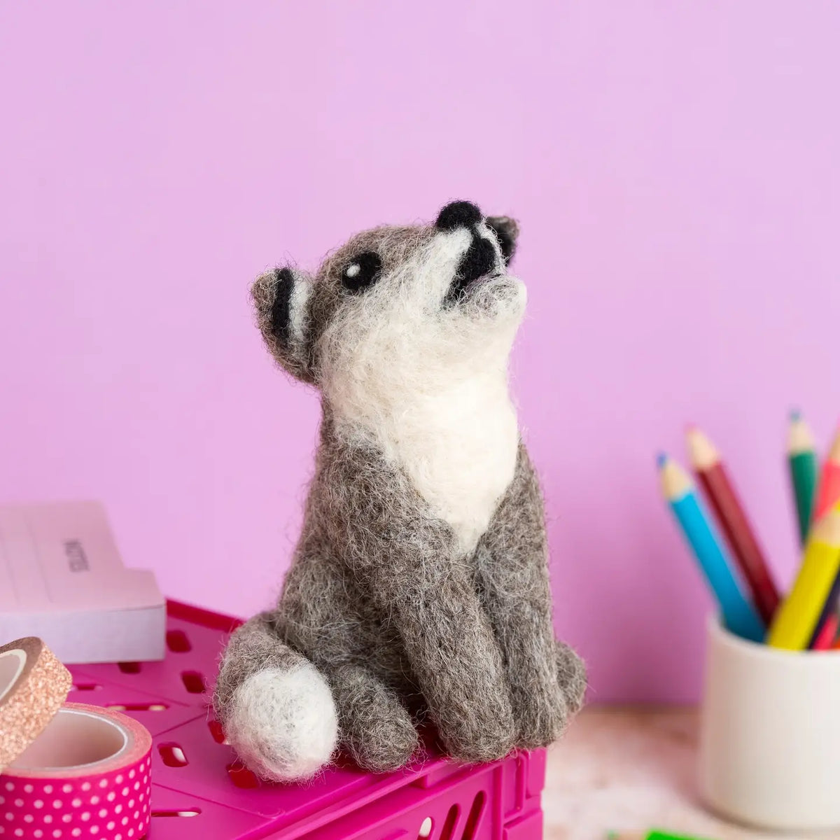 Needle felted wolf toy sitting on a pink surface with a light pink background