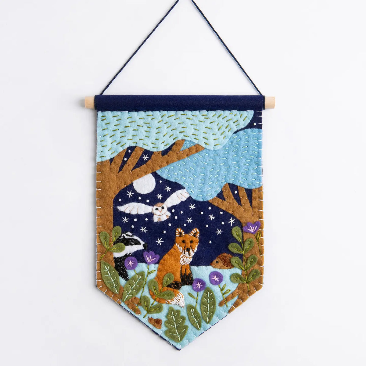 Felt pennant featuring trees, an owl, a fox, flowers, and a night sky hanging on a white background.