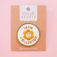 Iron-on patch with a flower design and 'Yarn Collector' text in paper packagingon a pink background