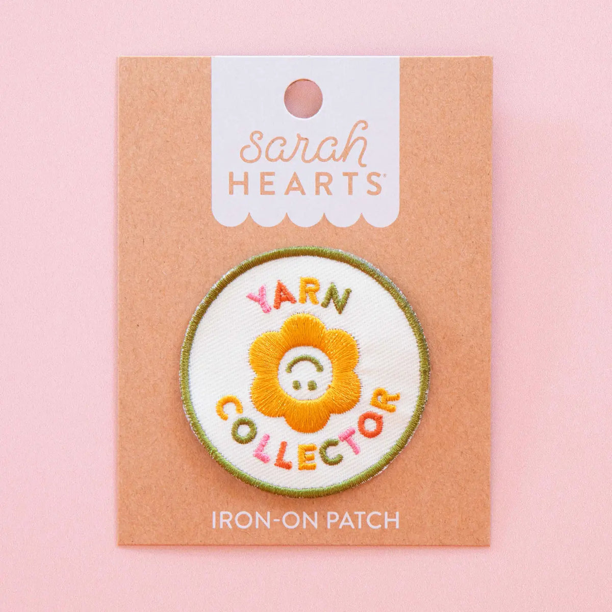 Iron-on patch with a flower design and 'Yarn Collector' text in paper packagingon a pink background