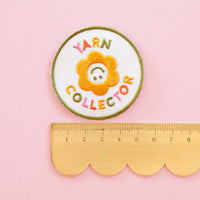 Embroidered patch with 'Yarn Collector' text and a flower design on a pink background, next to a ruler for scale.