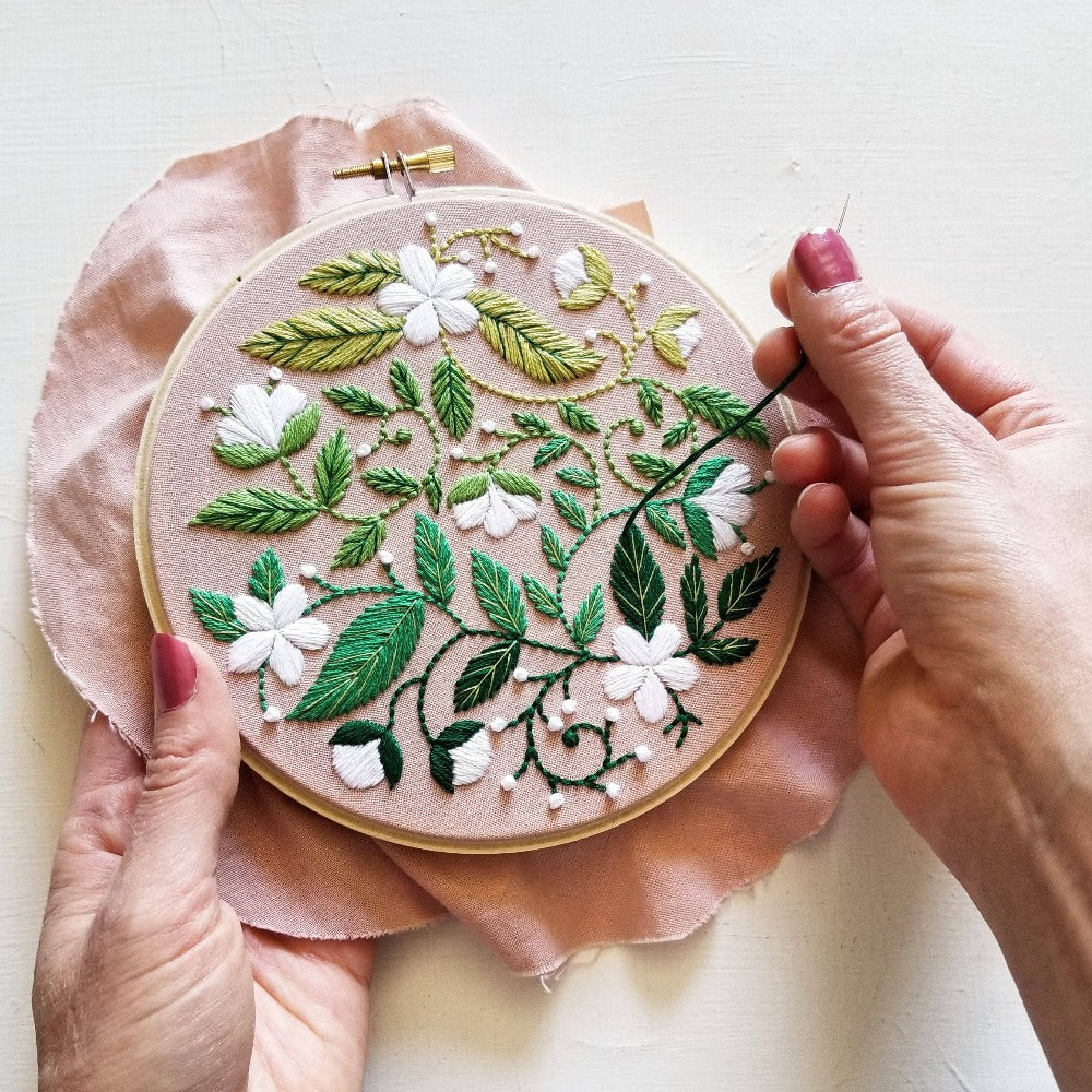 Blissful Blooms Beginner Embroidery Kit: an embroidery hoop with an elegant green and white floral embroidery design